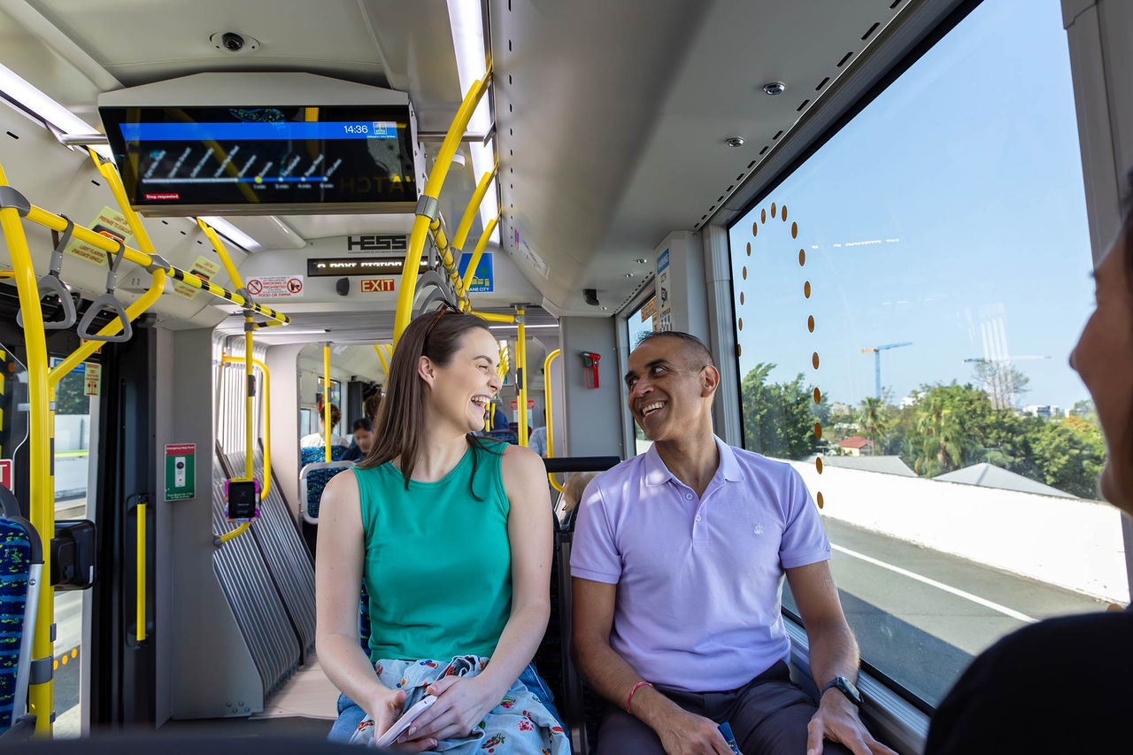 2 adult passengers sitting on a metro. Both passengers are talking and laughing.