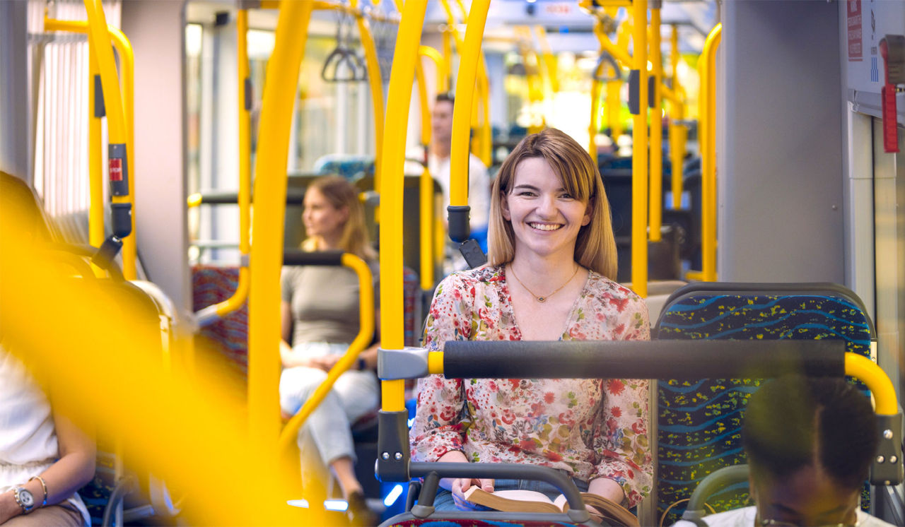 Female passenger onboard a metro, smiling with a book on her lap.